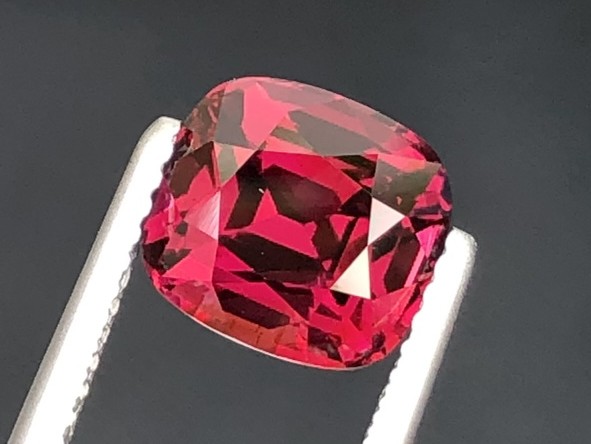 A red garnet from Tanzania, cushion cut, held in tweezers