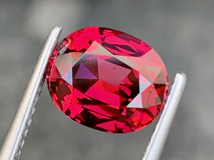 A red garnet from Tanzania, oval cut, held in tweezers