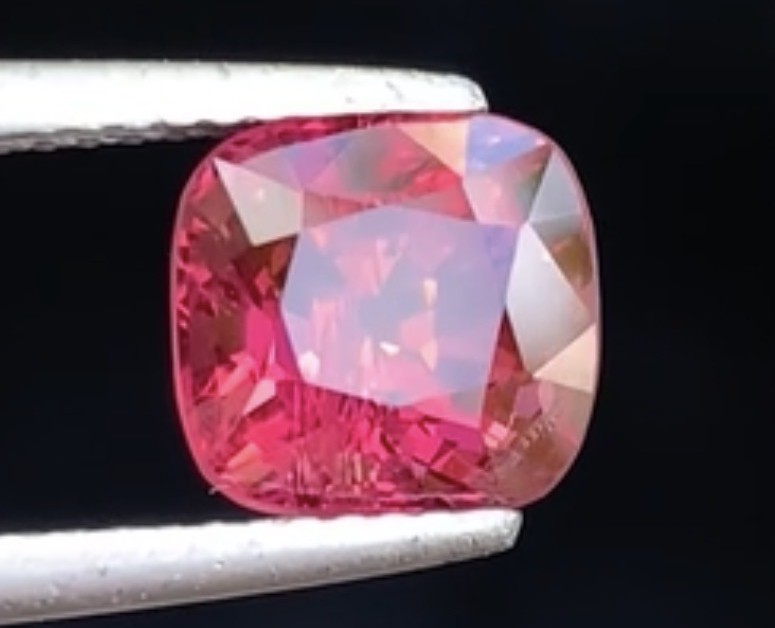 A pink spinel from Mahenge, Tanzania, cushion cut, held in tweezers